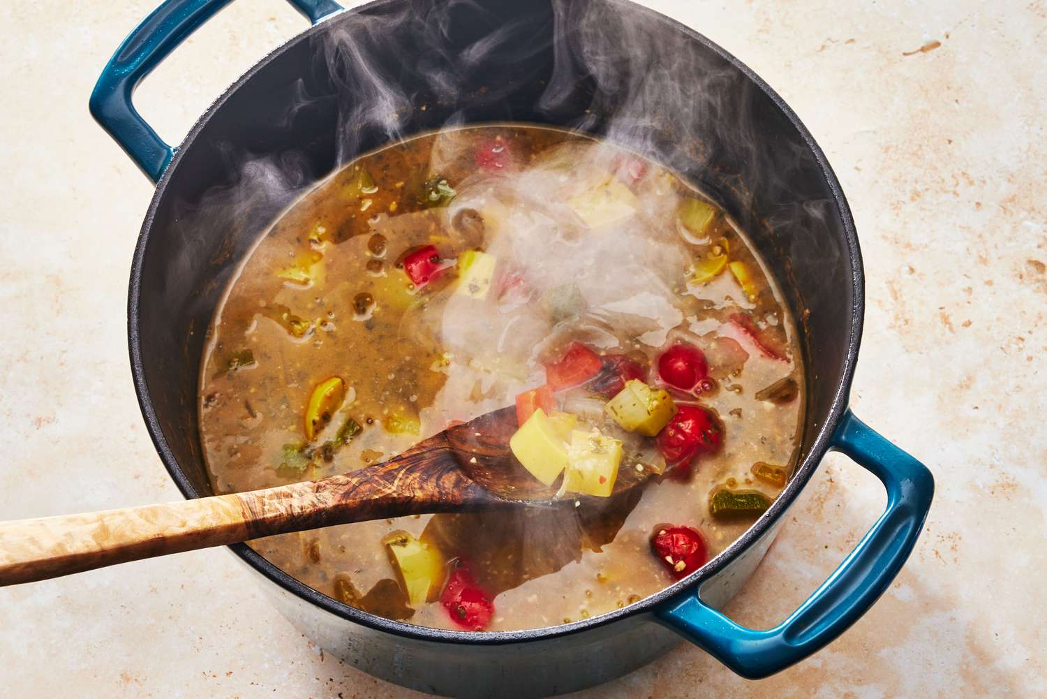 A Dutch oven on the stove with vegetable soup gently simmering, visible potatoes, carrots, beans, and herbs in a tomato broth