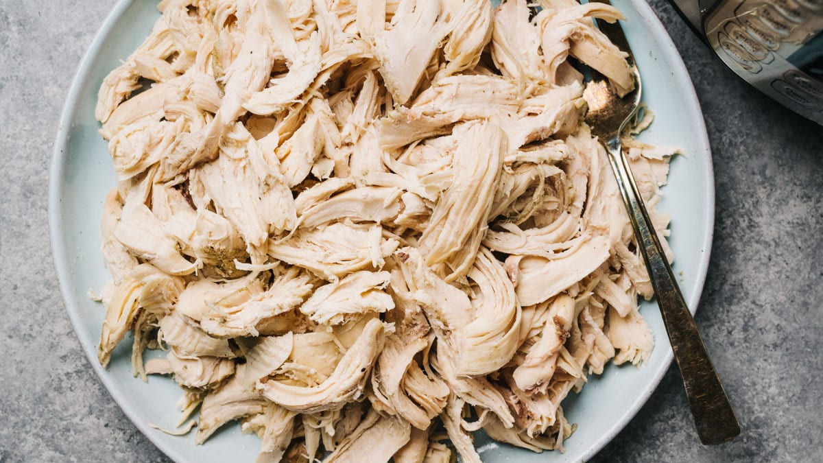 A bowl filled with shredded rotisserie chicken on a kitchen counter next to a cutting board and a chef's knife