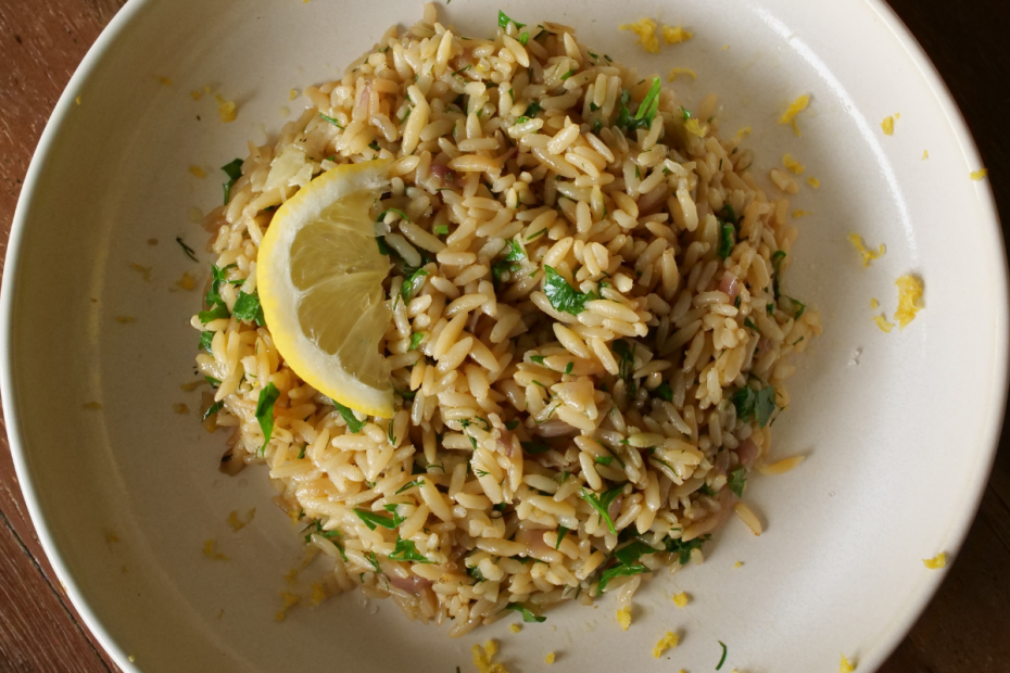 A bowl of cooked brown rice topped with chopped parsley and a lemon wedge on a wooden table