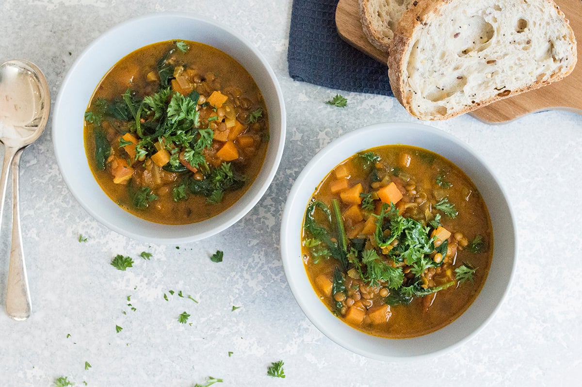 A bowl of hearty vegetable soup served with a slice of crusty bread on a linen napkin, set on a cozy dinner table