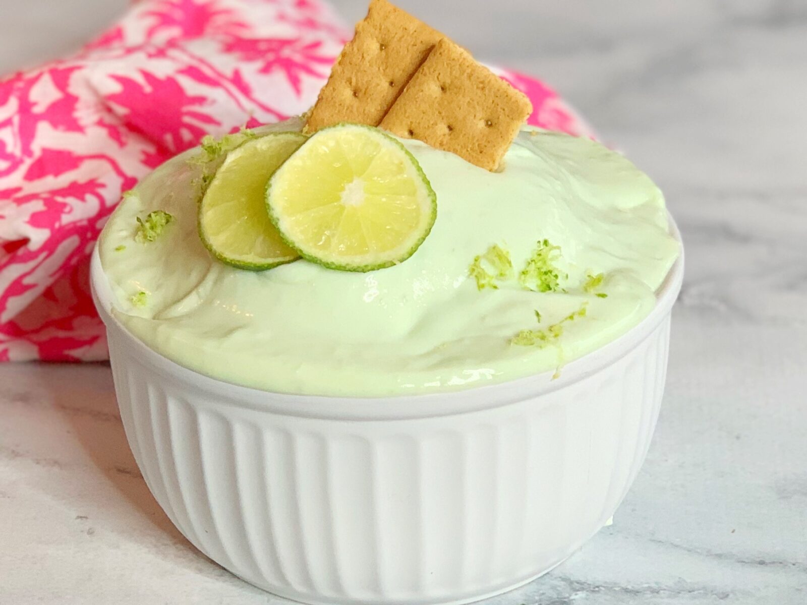A bowl of pale creamy sauce being whisked, with a halved lime and a can of sweetened condensed milk on a kitchen counter