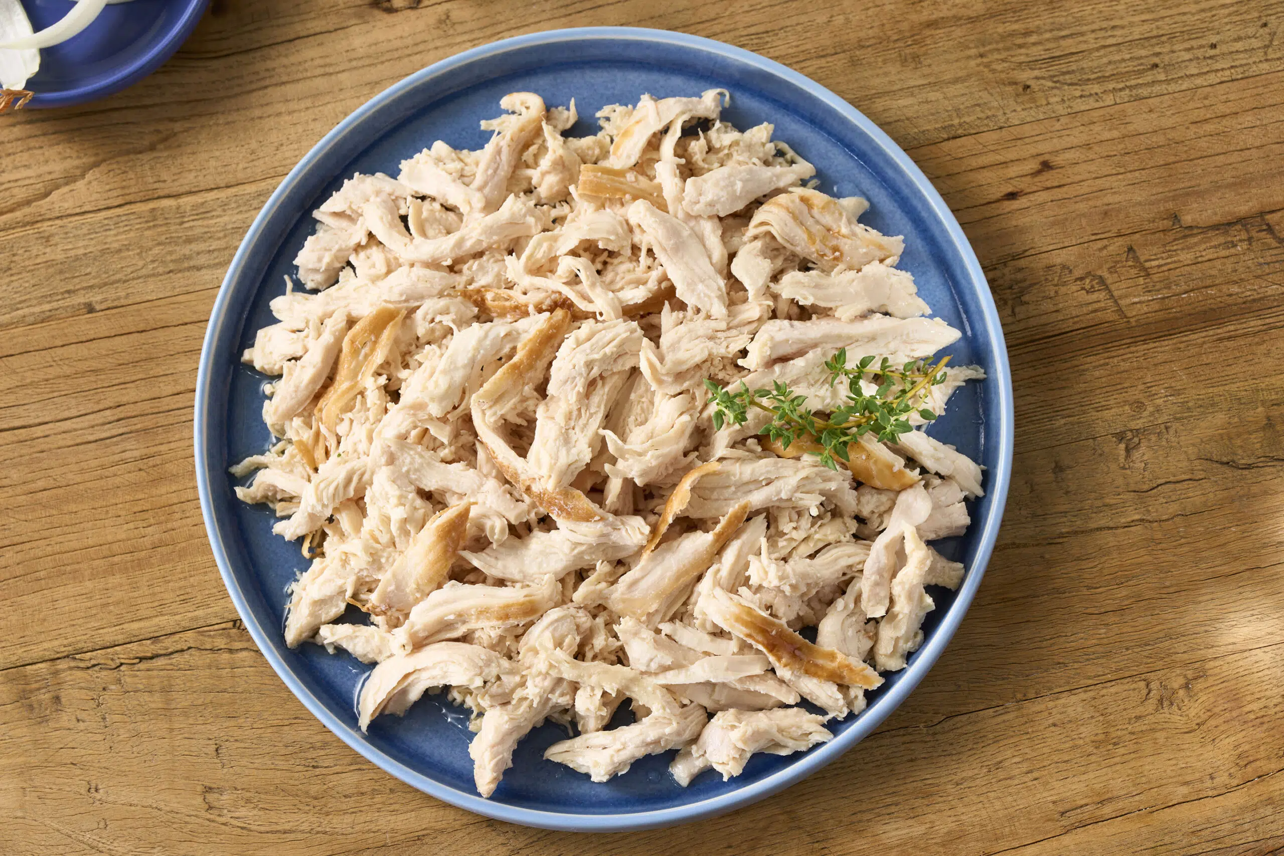 A bowl of shredded rotisserie chicken with two forks resting inside, set beside simple pantry ingredients on a kitchen counter