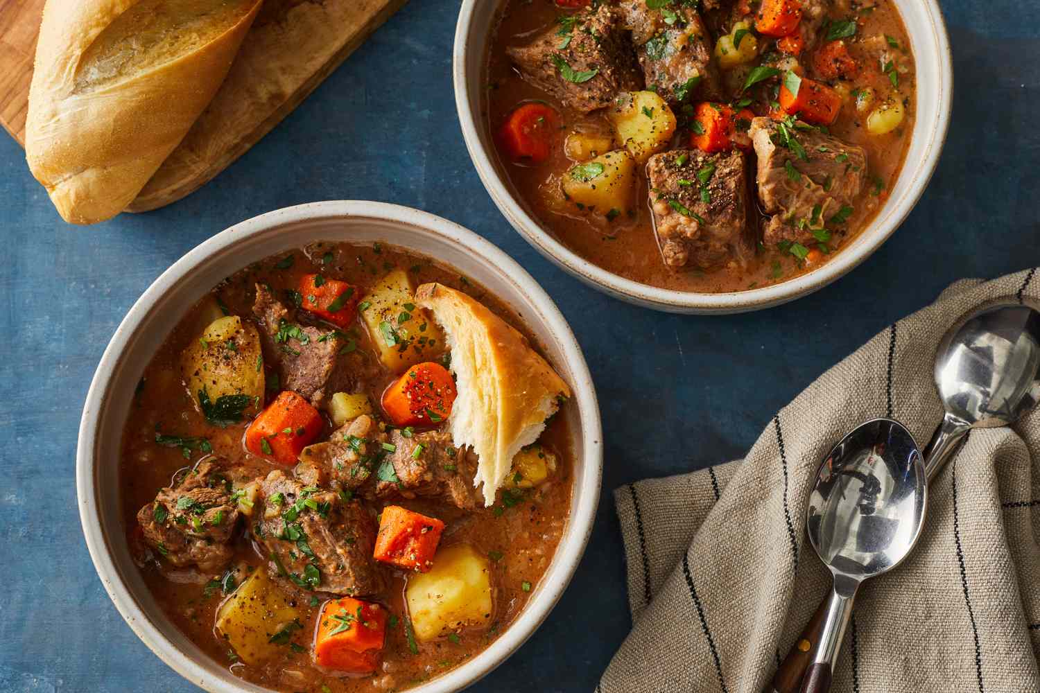 A bowl of slow cooker beef stew with tender beef chunks, carrots, and potatoes in a rich brown broth, set on a wooden table with a spoon beside it