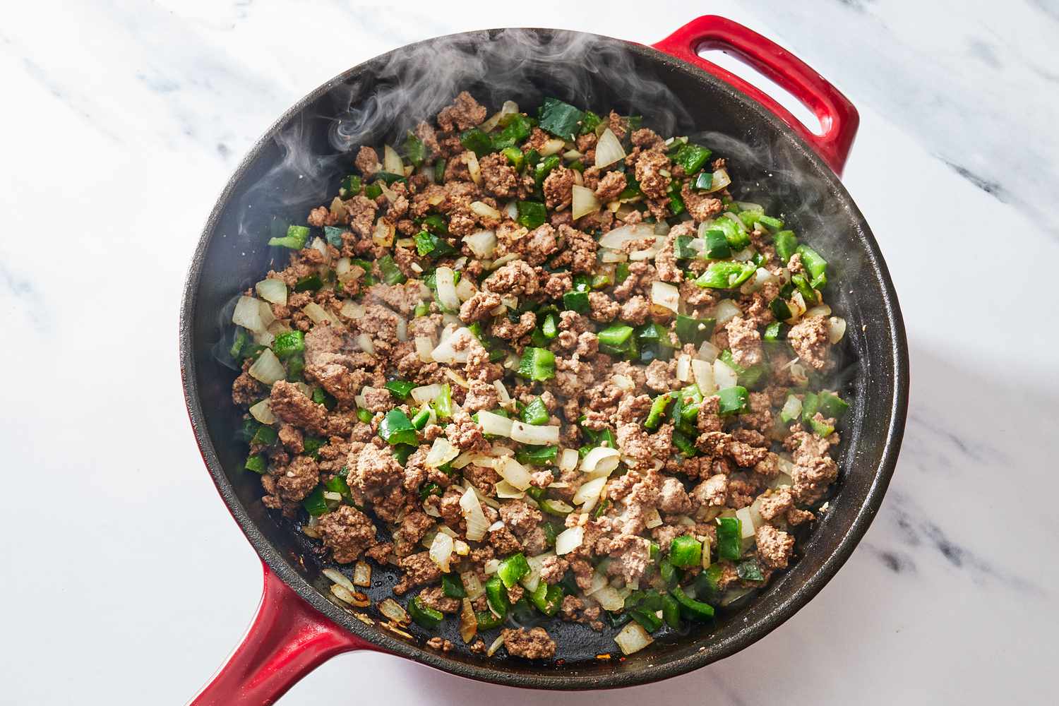 A cast iron skillet with browned ground beef being stirred as taco seasoning and a splash of water simmer into a glossy sauce