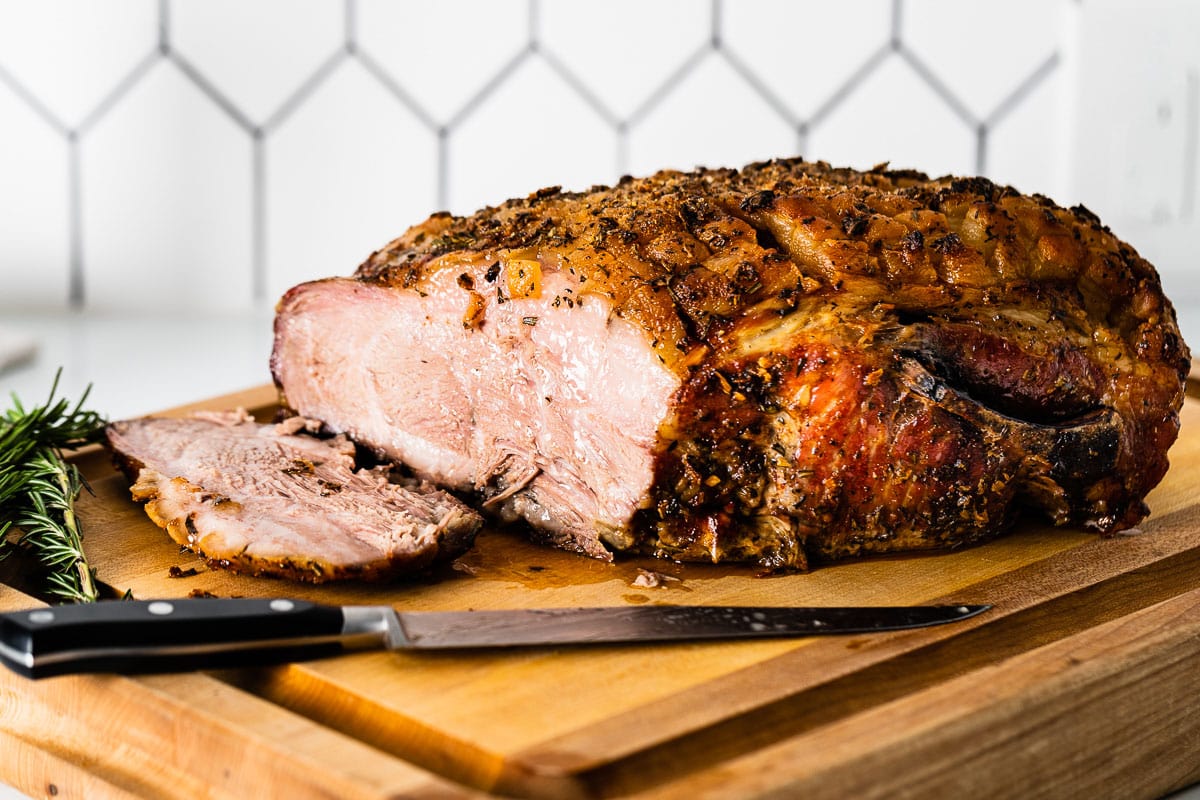 A cooked pork roast resting on a wooden cutting board with juices pooling lightly while the slow cooker sits nearby