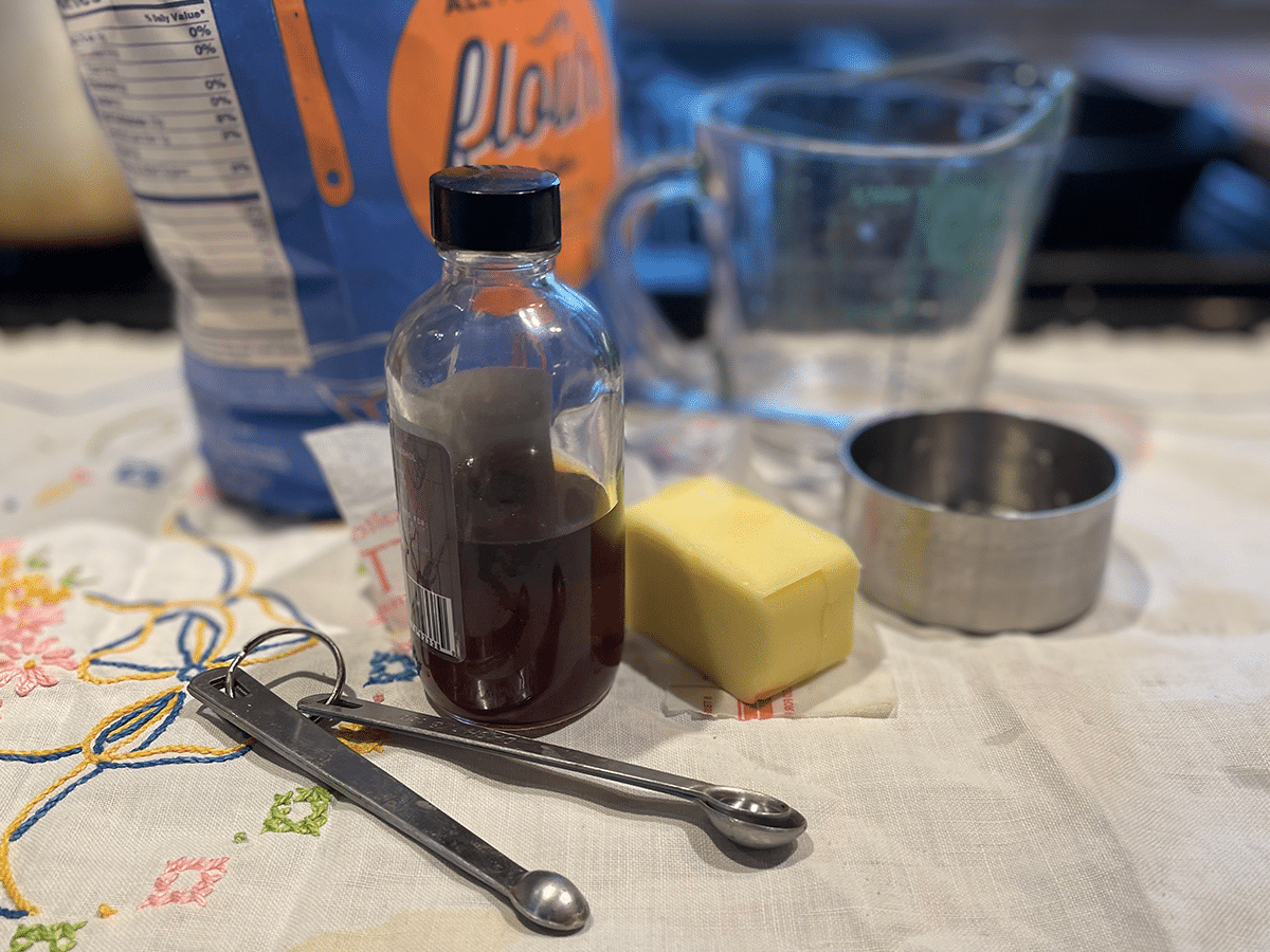 A countertop with measured flour, sugar, butter, eggs, milk, and a bottle of vanilla extract set up for baking vanilla cake