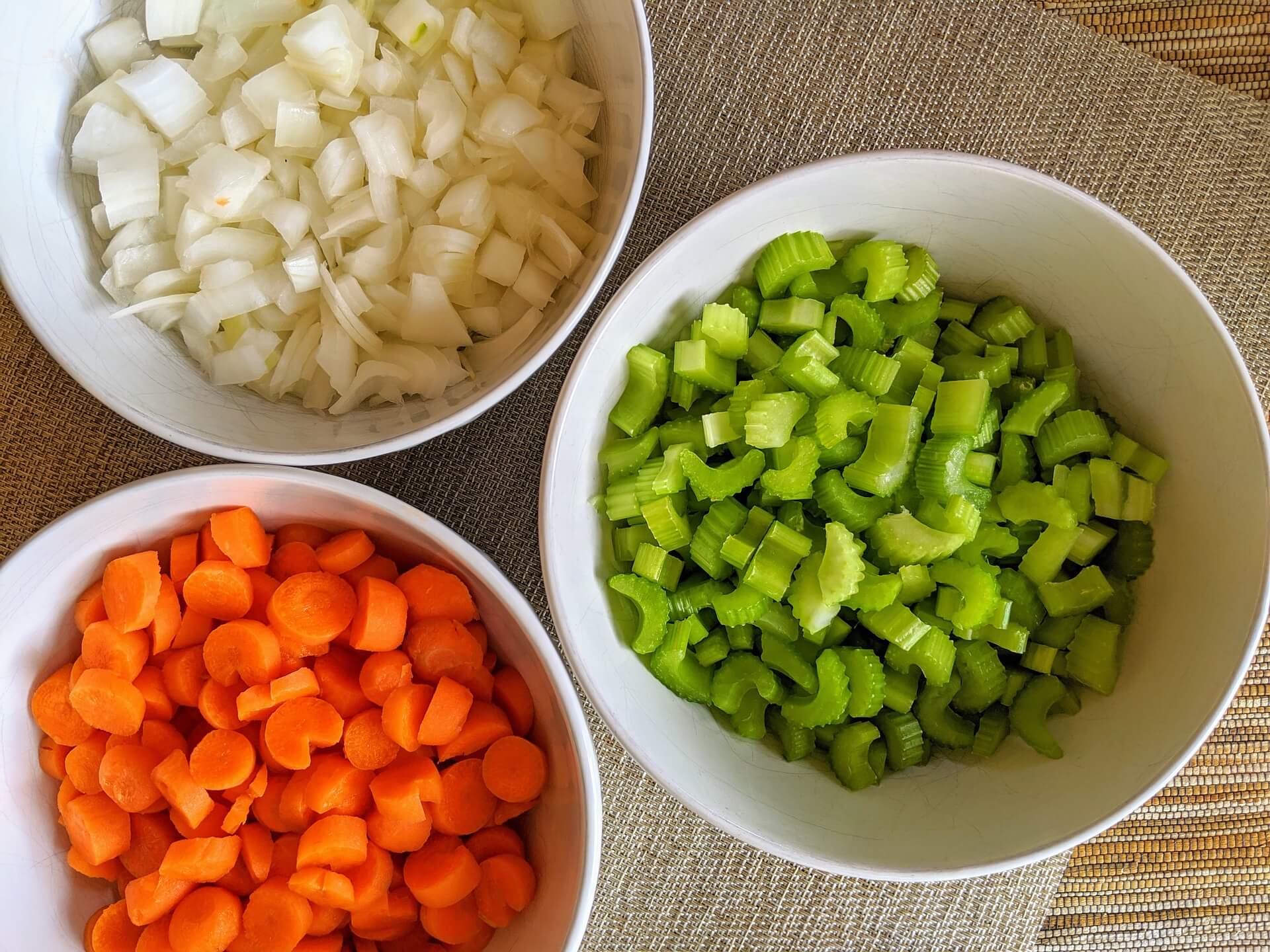 A cutting board with neatly chopped onion, celery, and green bell pepper next to a chef's knife, ready for cooking