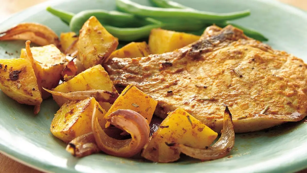 A dinner plate with sliced pork chops topped with pan sauce served next to roasted golden potatoes and a small pile of sautéed greens