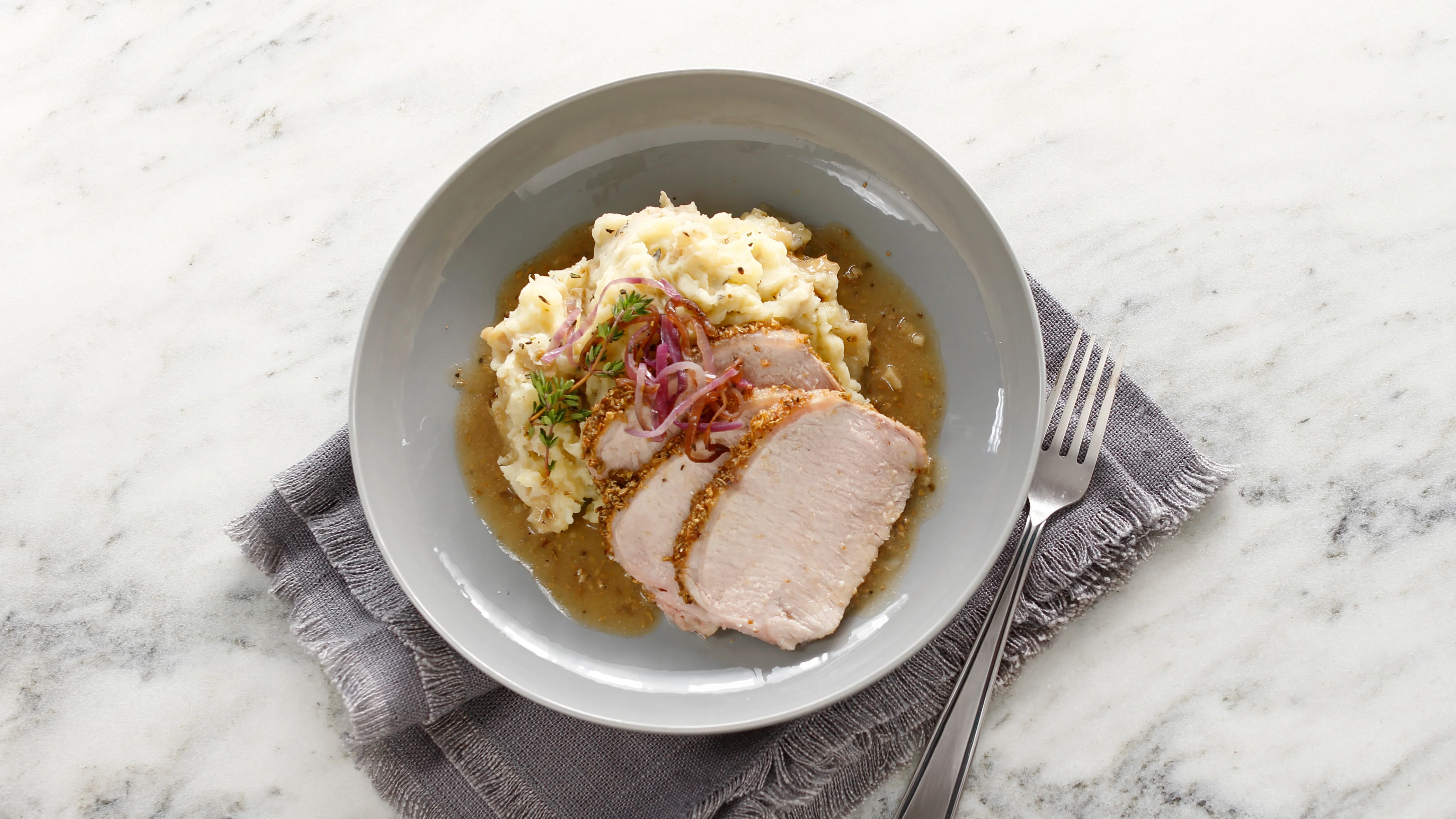 A dinner plate with sliced pork roast covered in gravy beside mashed potatoes and green beans