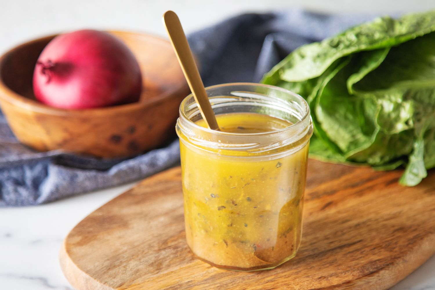 A glass jar of homemade Italian dressing with visible herbs and minced garlic, sitting next to a small whisk and a vinegar bottle on a kitchen counter