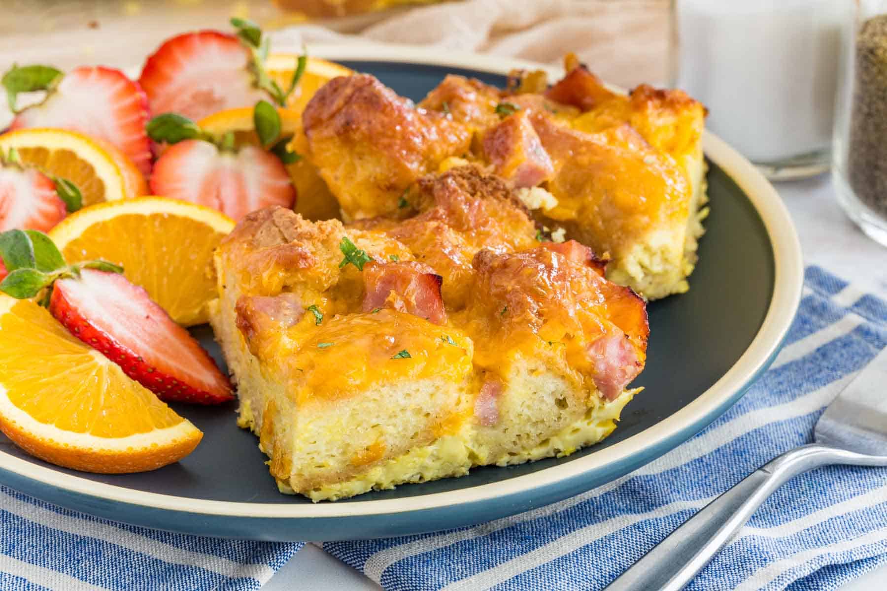 A golden-brown slice of gluten-free breakfast casserole on a plate with visible layers of egg, roasted vegetables, and melted cheese, with a baking dish behind it