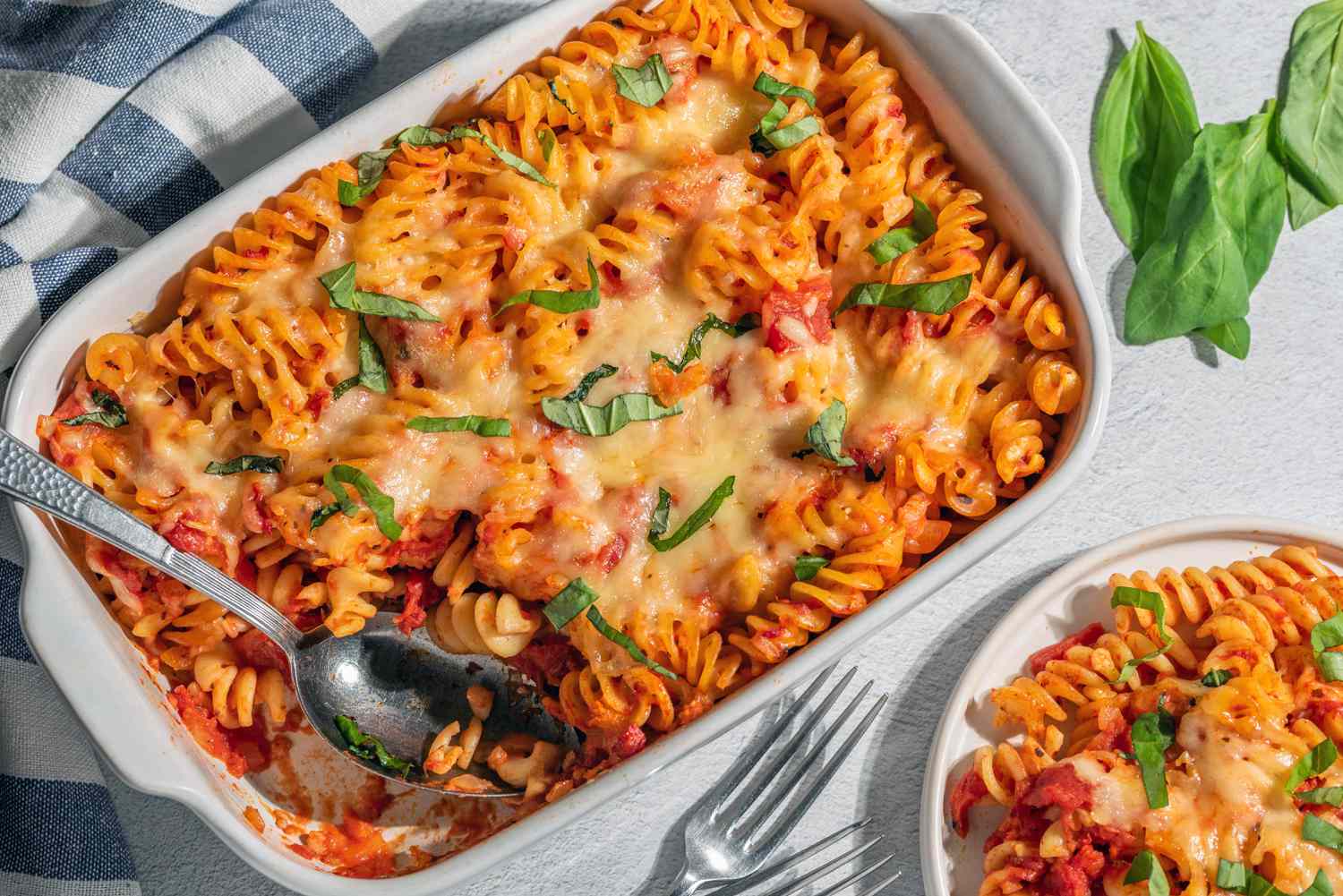 A golden, bubbly baked pasta casserole in a white baking dish with browned cheese on top and a spoon scooping out a saucy portion