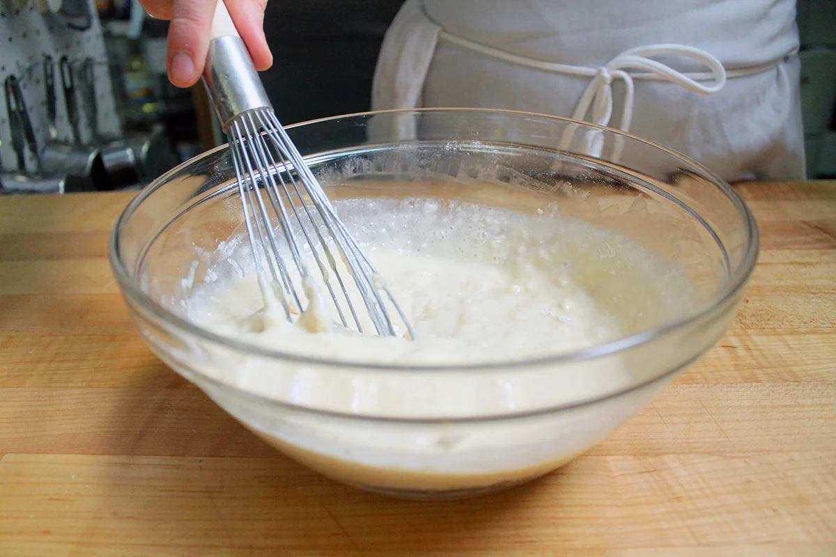 A large ceramic bowl with flour, sugar, baking powder, and salt being whisked together to make homemade pancake mix