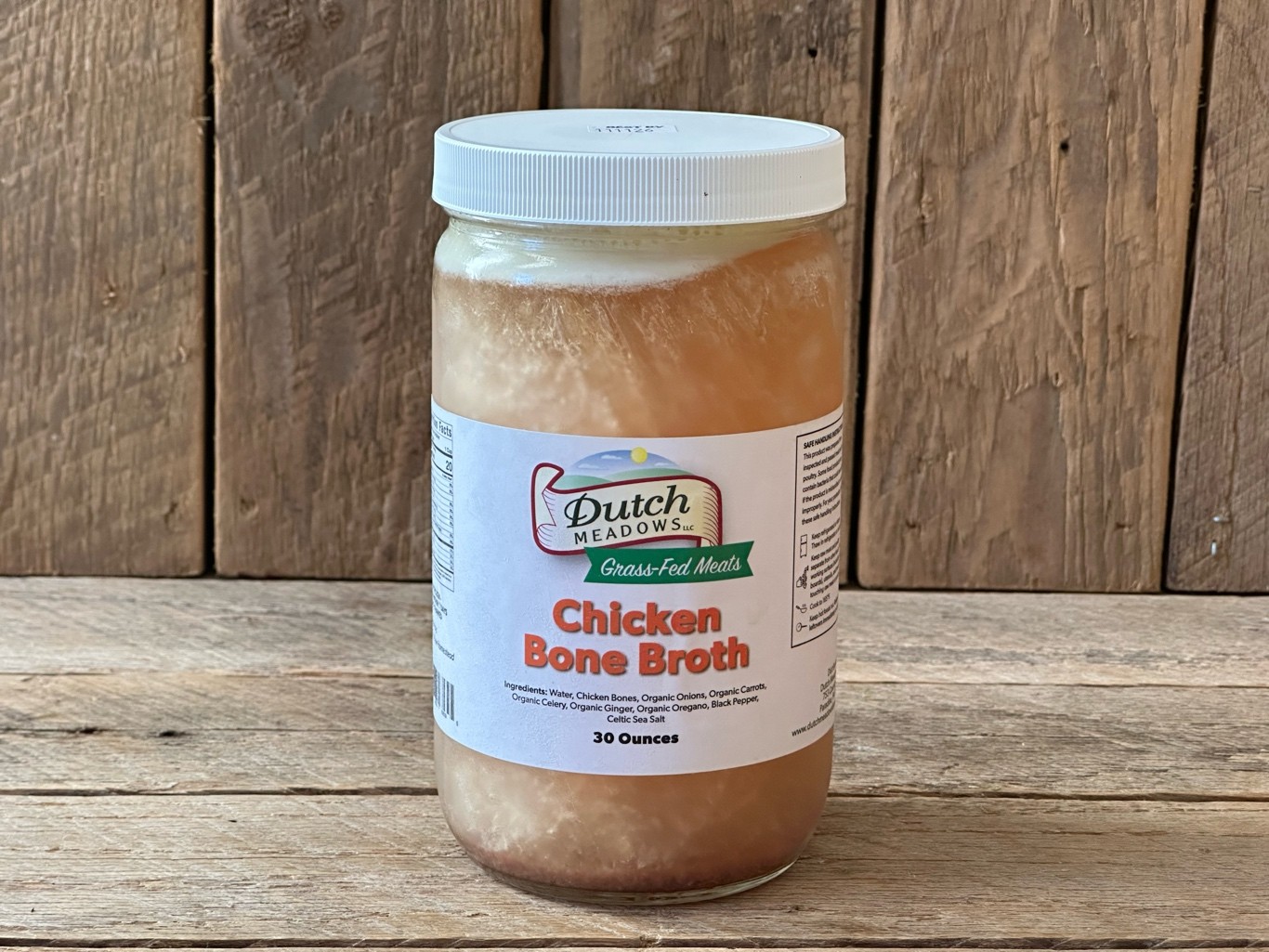 A mason jar filled with golden chicken bone broth on a kitchen counter, with a visible layer of set gel and a small bowl of shredded chicken nearby