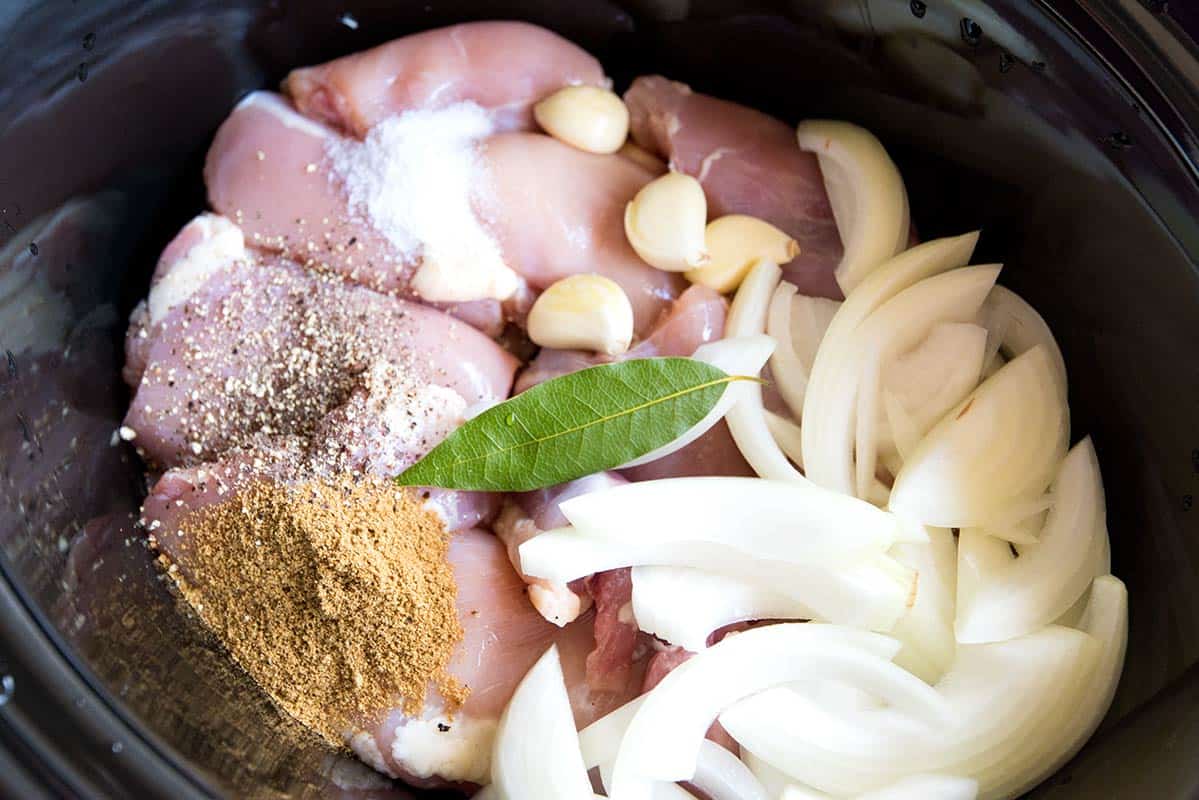 A pair of forks shredding tender cooked chicken inside a slow cooker filled with broth and vegetables
