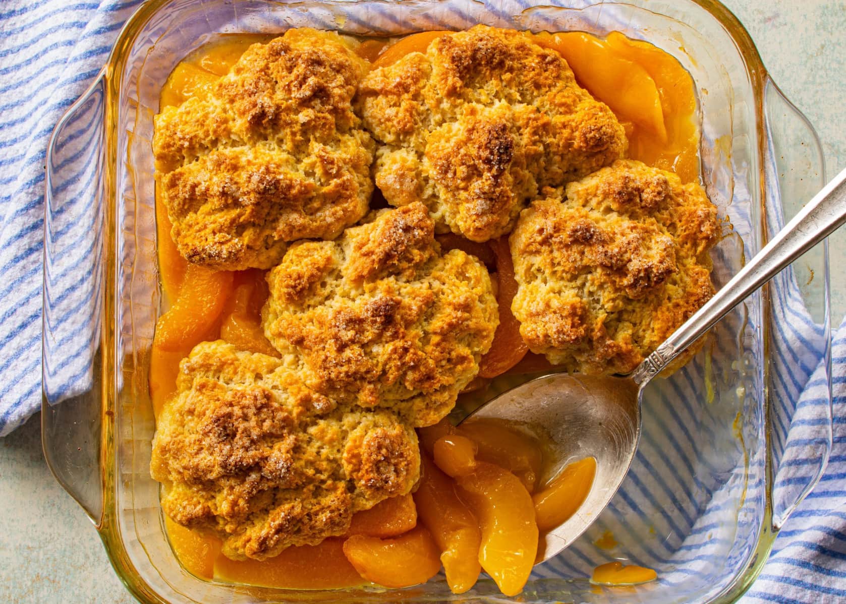 A peach cobbler baking in a glass dish with bubbling fruit and a golden crust visible through an open oven door