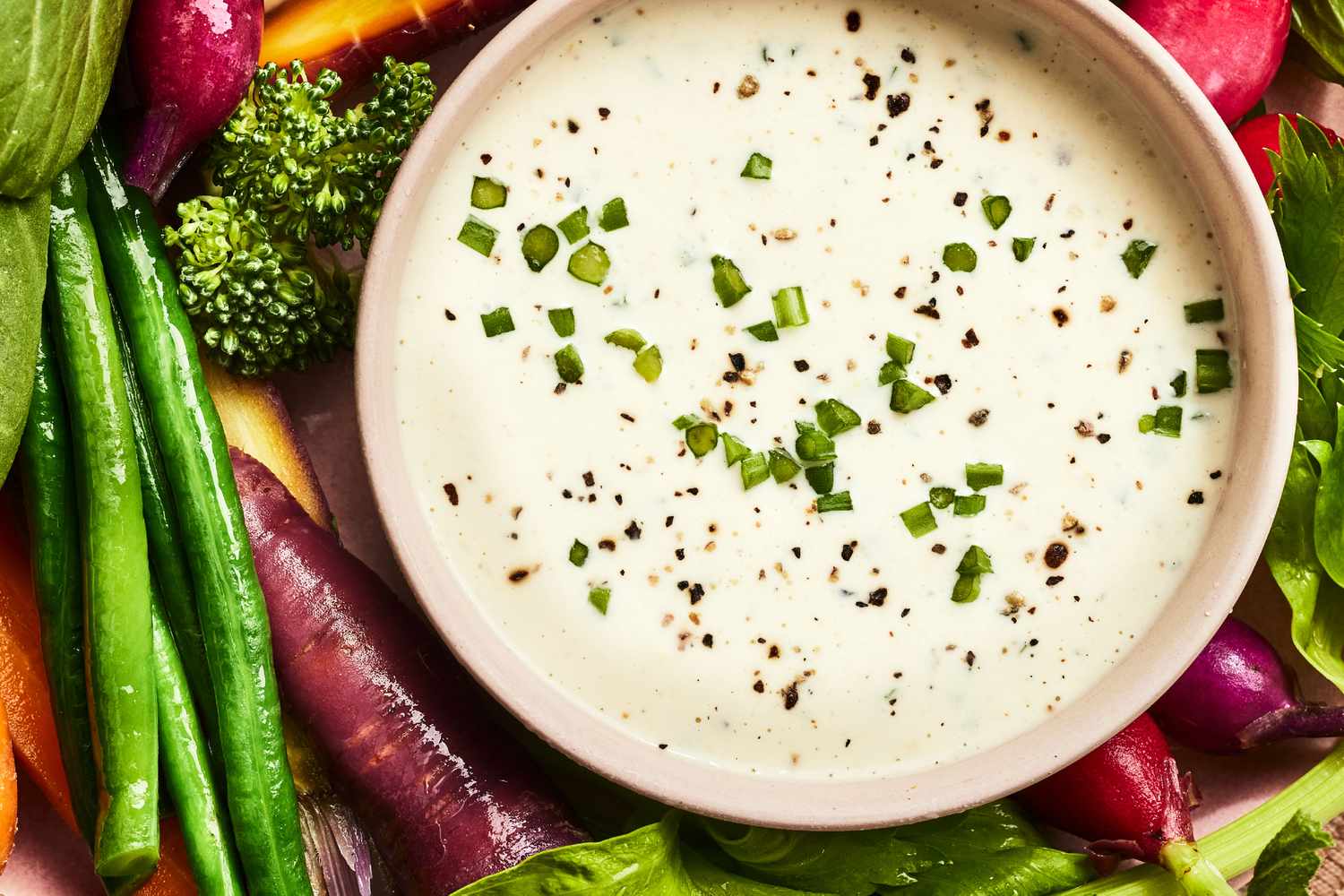 A real photograph of ranch dip in a small bowl topped with chopped fresh chives, with a spoon resting beside it on a countertop