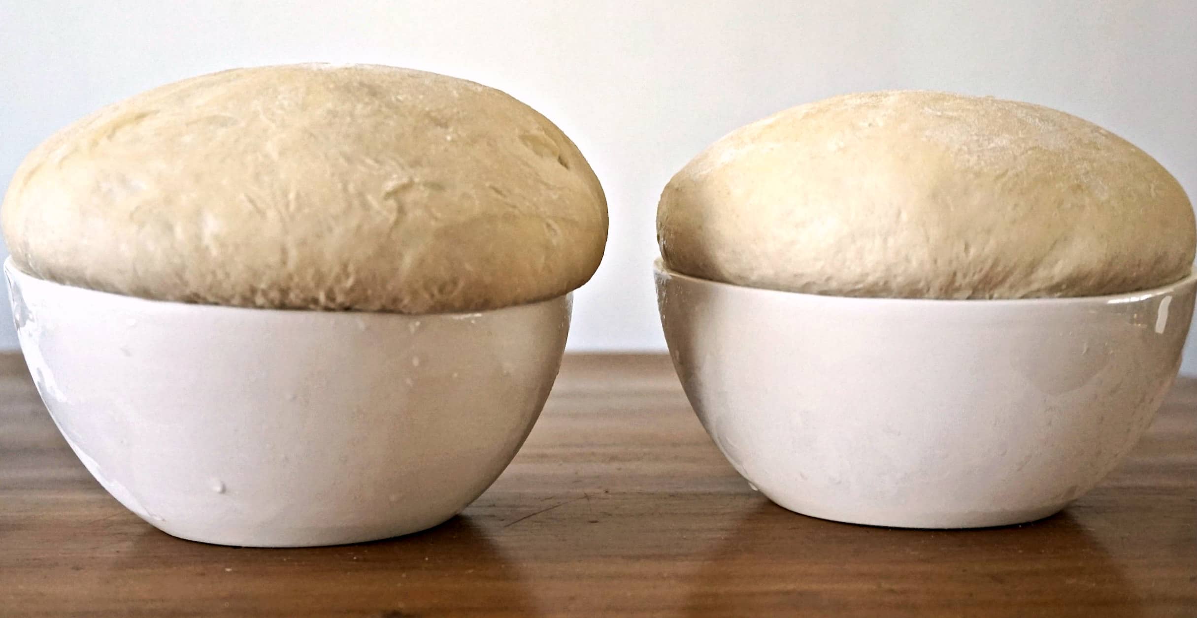 A risen pizza dough in a mixing bowl that has doubled in size, with a soft domed surface and small bubbles under the skin