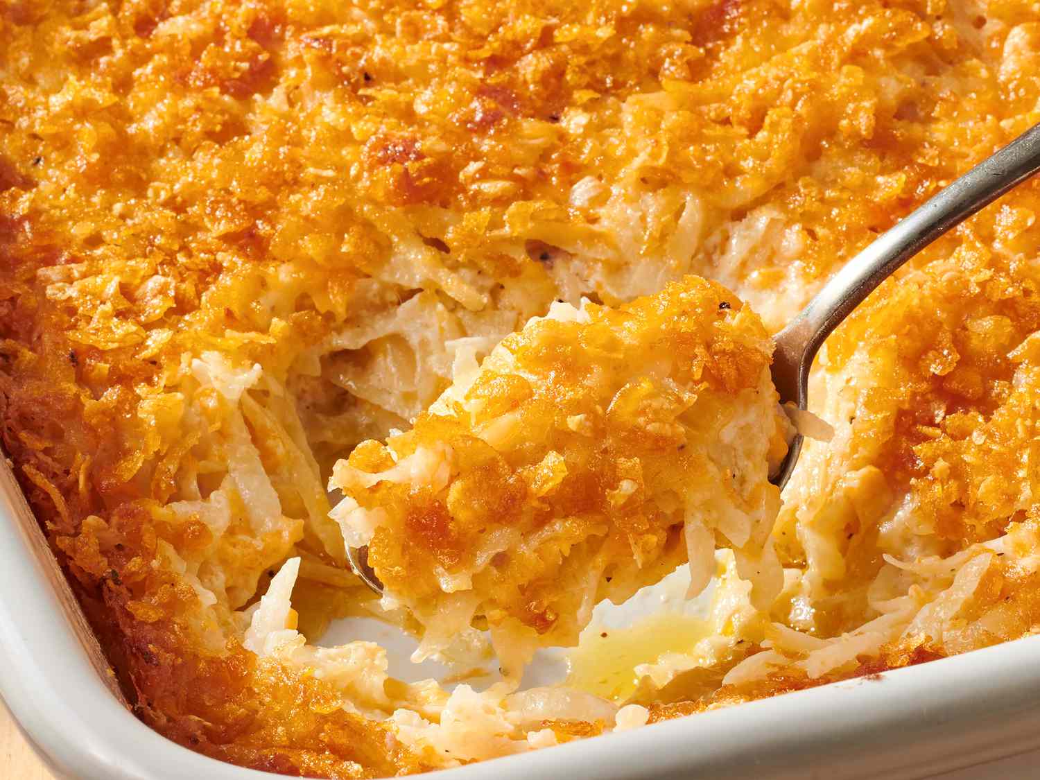 A serving of cheesy potato casserole on a dinner plate beside roasted meat and green vegetables on a warmly lit dining table