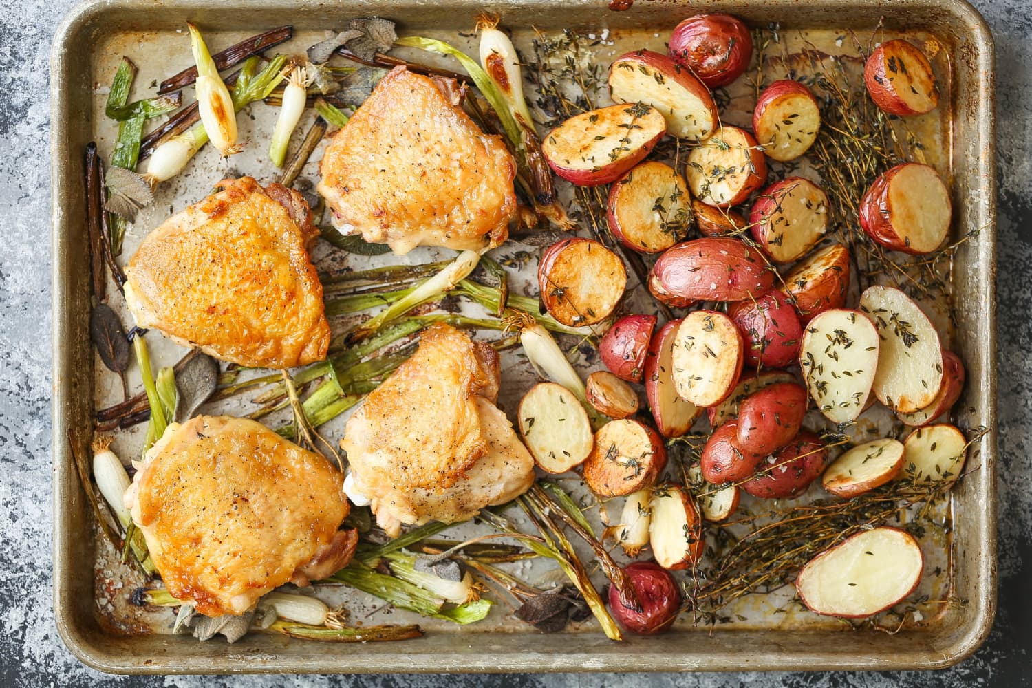 A sheet pan filled with golden roasted chicken thighs, halved baby potatoes, and bright green beans, fresh from the oven on a kitchen counter
