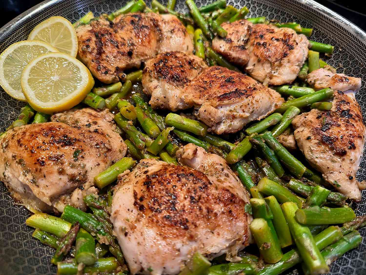 A skillet filled with lemon garlic chicken pieces nestled into fluffy rice with wilted greens and lemon slices on a kitchen counter
