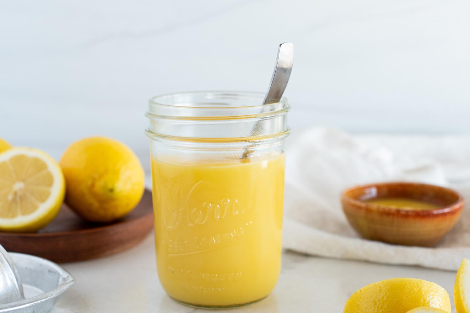 A small glass jar filled with glossy savory lemon curd on a wooden cutting board, with fresh lemons and a few thyme sprigs nearby in natural window light