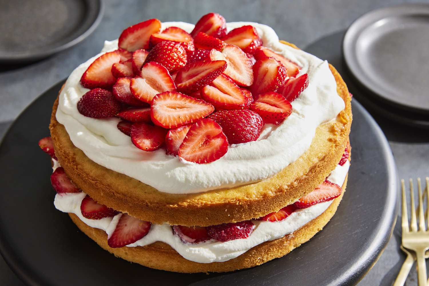 A spoonful of vanilla whipped cream being dolloped onto a bowl of fresh strawberries on a wooden table in natural light