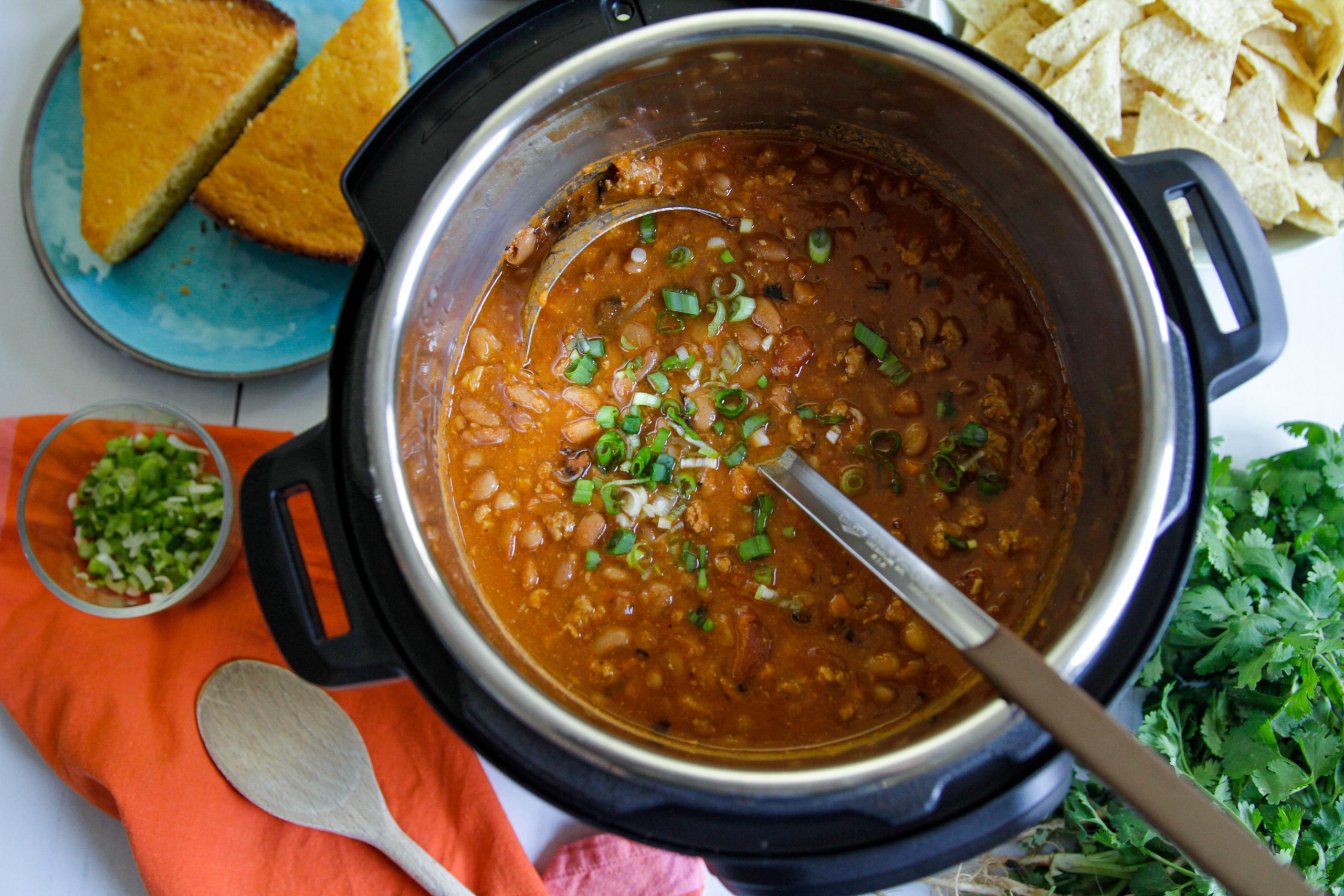 A stainless steel Instant Pot insert filled with beef and bean chili, steam rising as a ladle lifts a scoop showing thick texture and visible beans