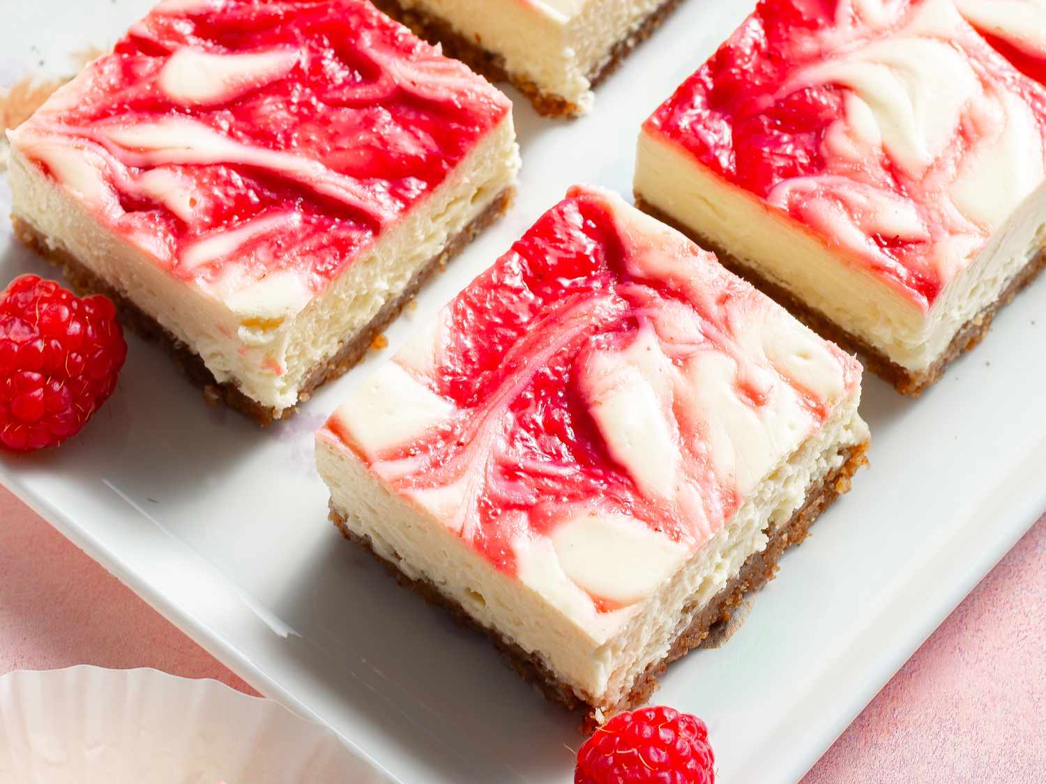A whole raspberry swirl cheesecake on a cake stand with several cleanly cut slices, showing a smooth top and defined graham cracker crust