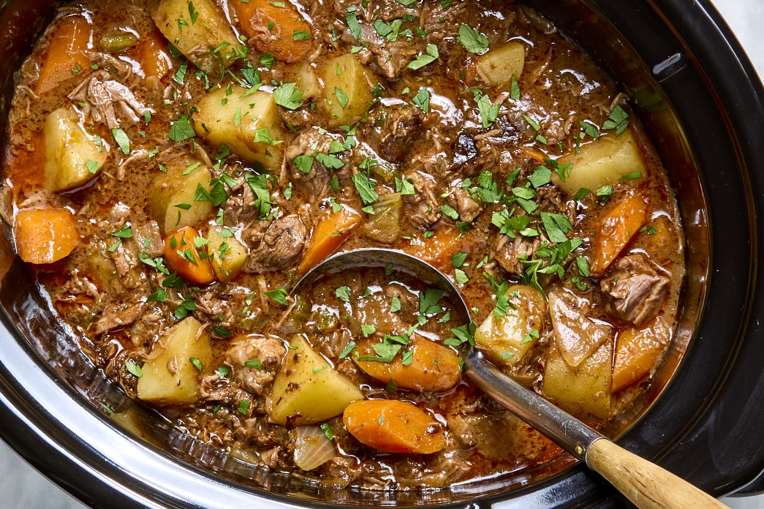 Beef stew cooking inside a slow cooker with visible chunks of beef, carrots, and potatoes in a rich broth