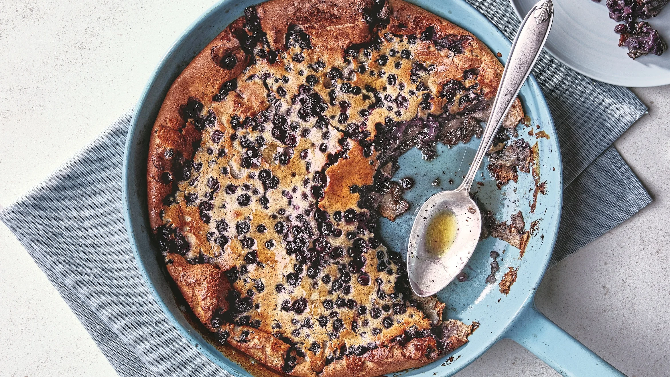 Blueberry pancake batter cooking in a cast iron skillet with blueberries scattered on top before flipping