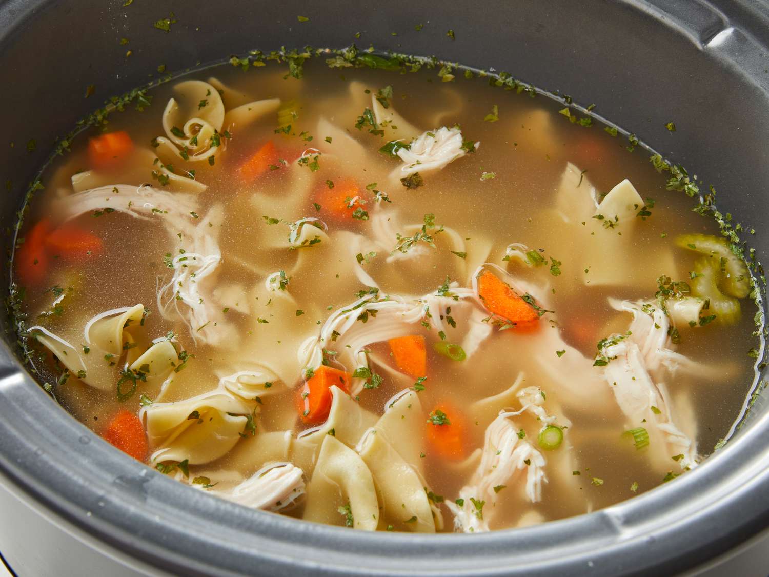 Chicken broth, raw chicken thighs, chopped carrots, celery, onion, garlic, bay leaves, and egg noodles arranged and ready for cooking