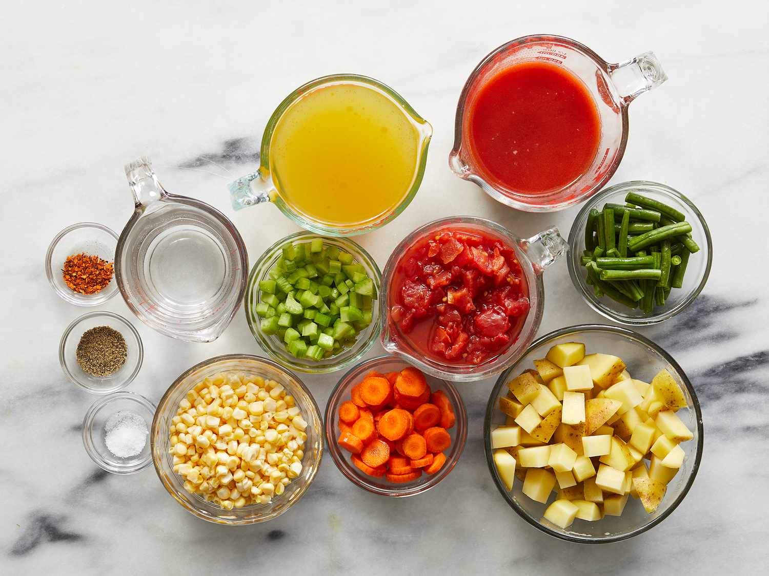 Chopped onions, carrots, celery, potatoes, and green beans arranged on a wooden cutting board next to a Dutch oven on a kitchen counter