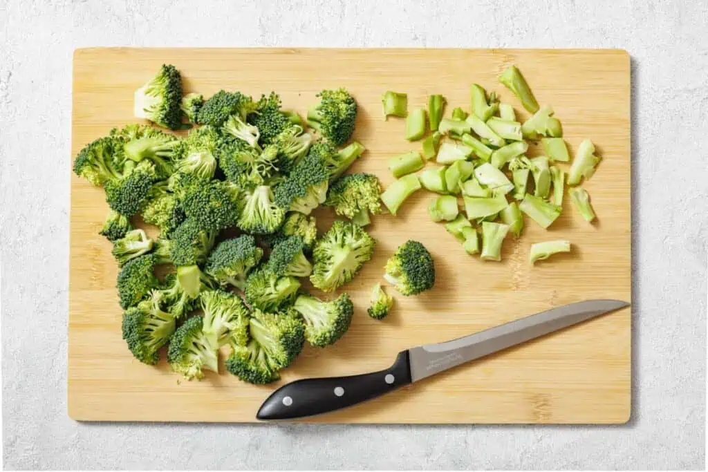 Fresh broccoli florets and thinly sliced broccoli stems on a cutting board with a chef’s knife, ready for salad prep