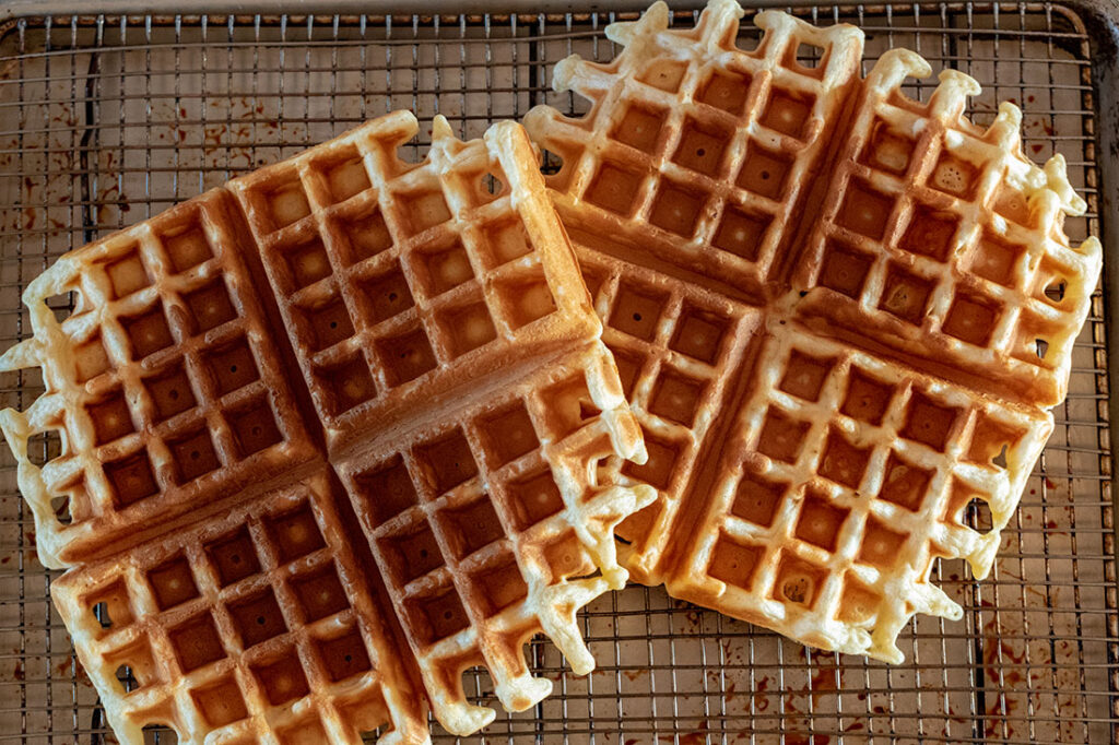 Freshly cooked golden waffles cooling on a wire rack set over a baking sheet in a home kitchen