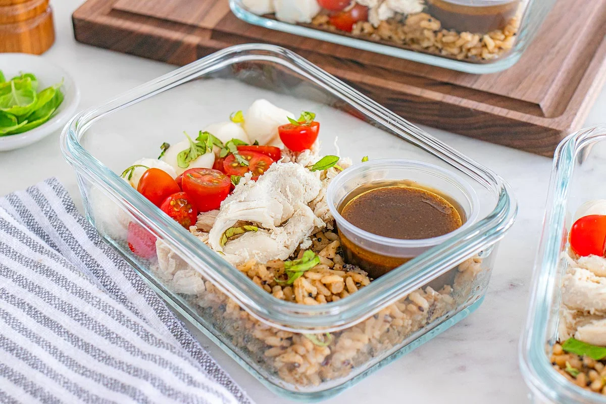 Glass meal prep containers filled with cooked brown rice and roasted vegetables on a kitchen counter