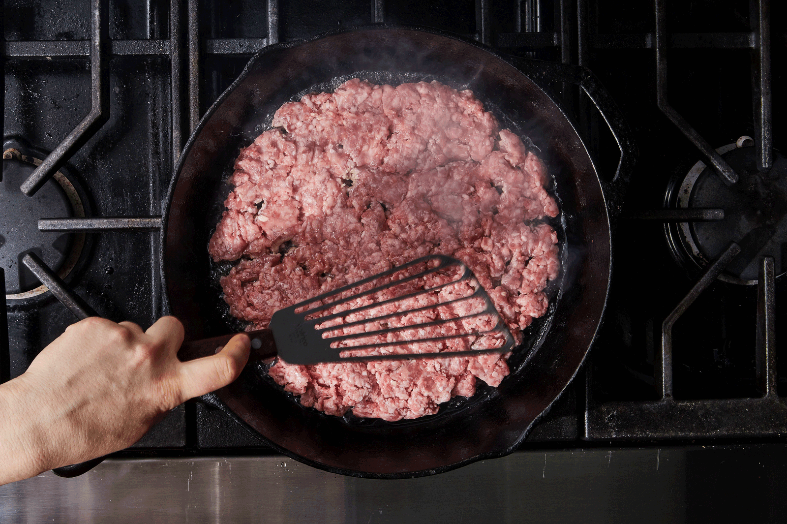 Ground beef browning in a wide saucepan with onion and tomato paste being stirred with a wooden spoon