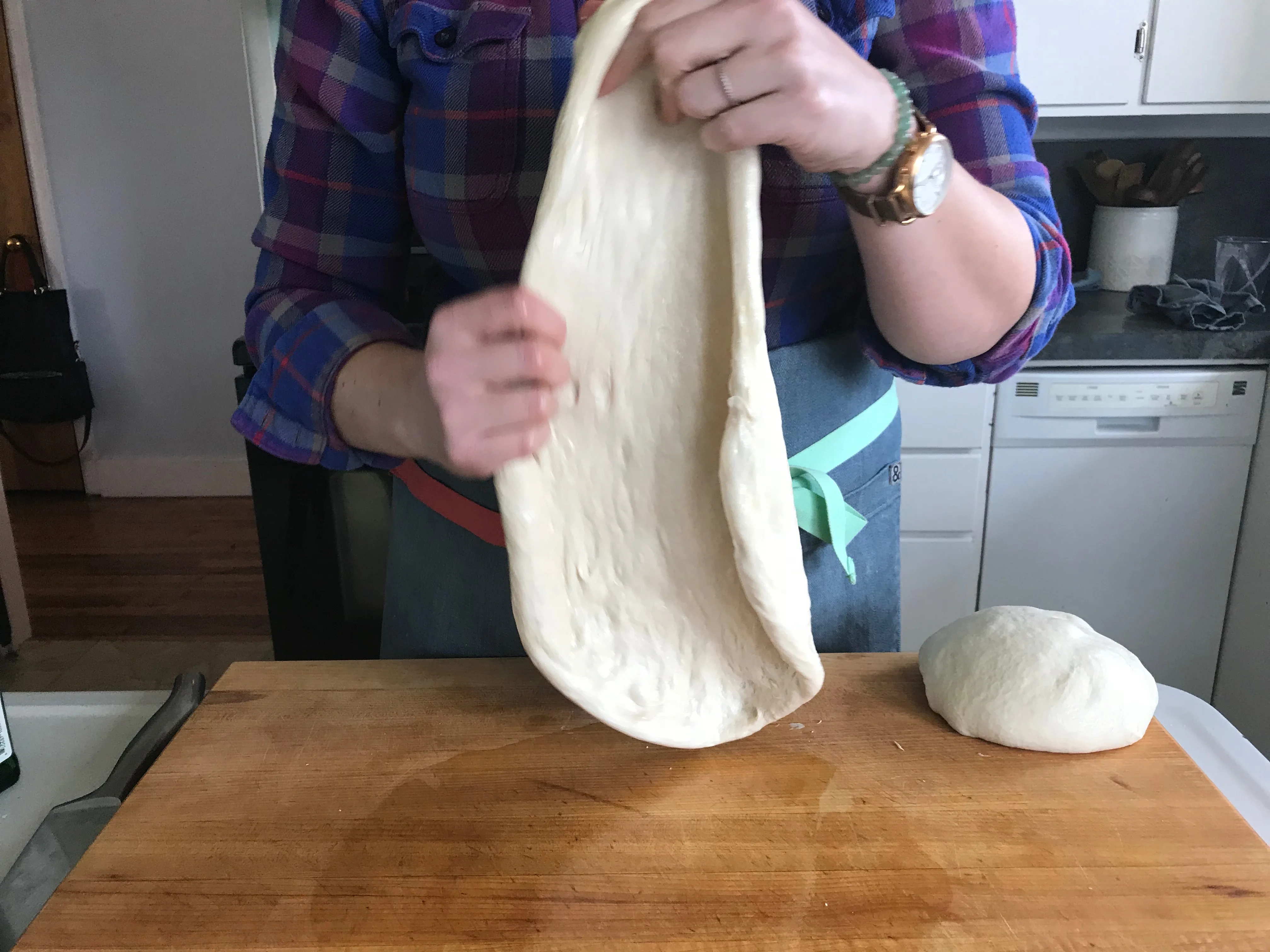 Hands gently stretching pizza dough over knuckles on a kitchen counter, with the dough forming a thin round and a thicker rim