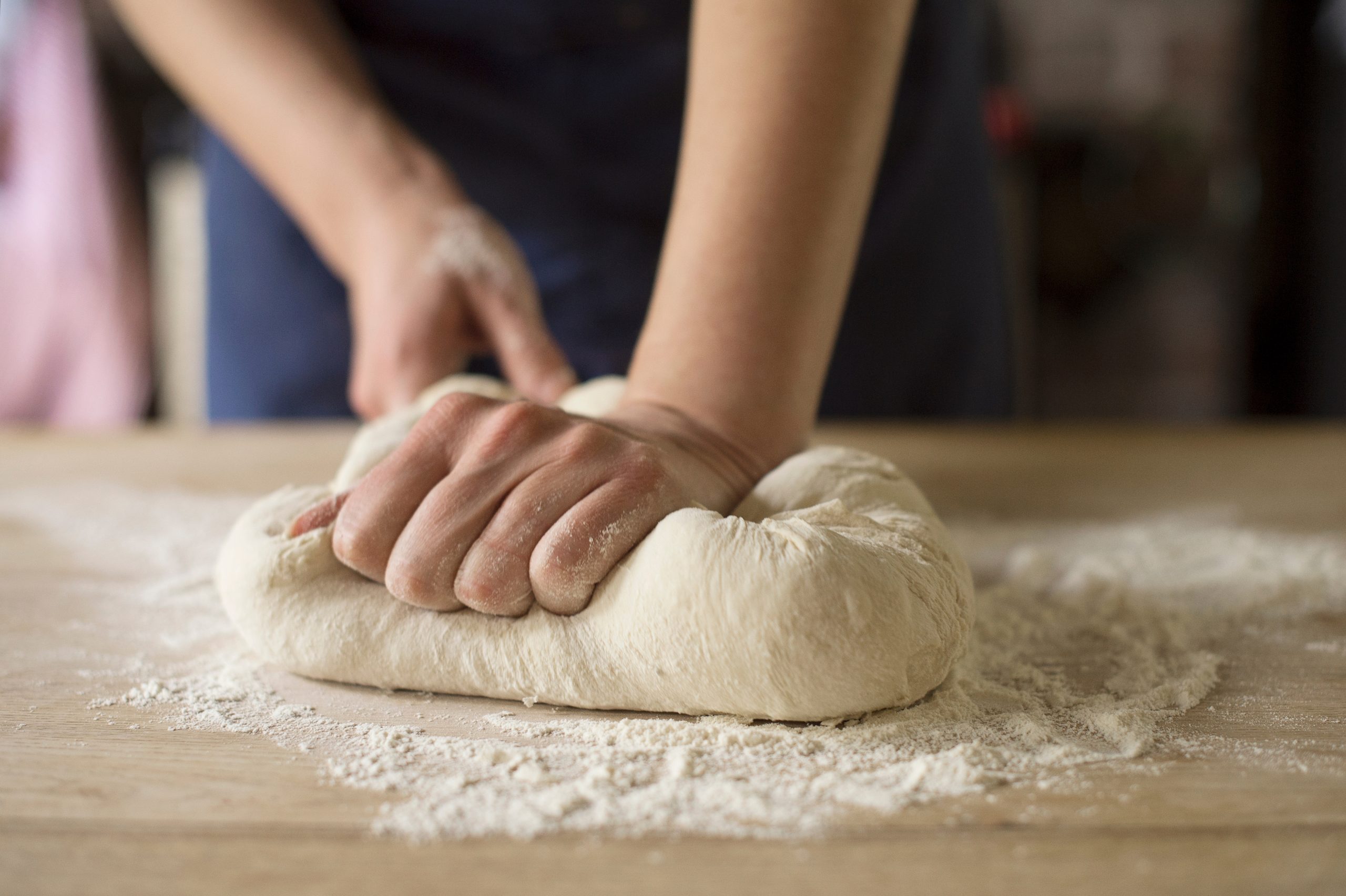 Hands kneading a soft yeast dough on a lightly floured countertop, with the dough being folded and pressed into a smooth, elastic ball