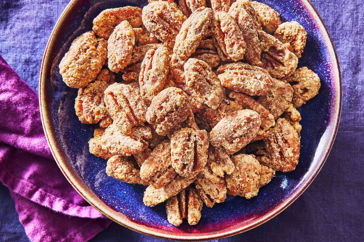 Pecan halves, a bowl of granulated sugar, a small pat of butter, and a bottle of vanilla extract arranged on a kitchen counter