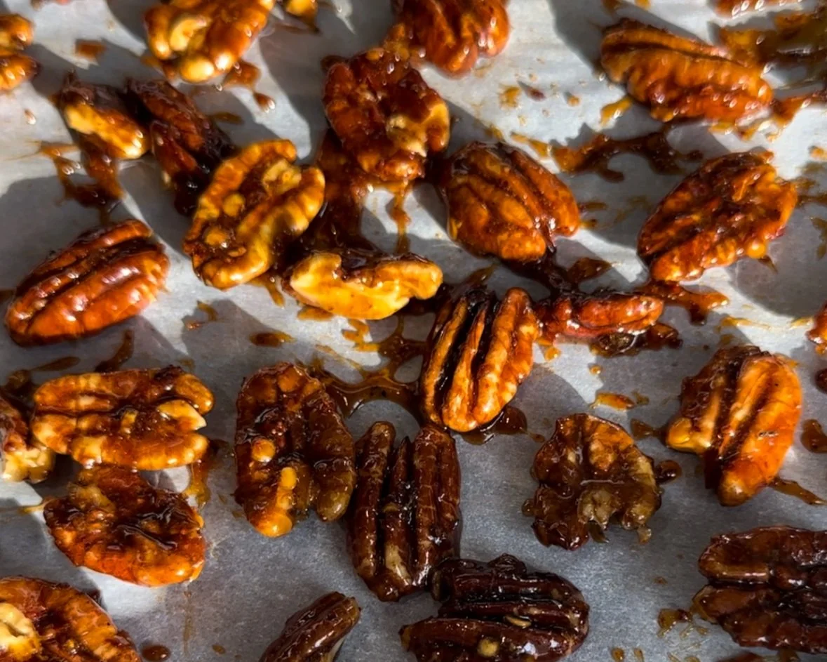 Pecans coated with sugar and spices roasting on a rimmed baking sheet inside an oven