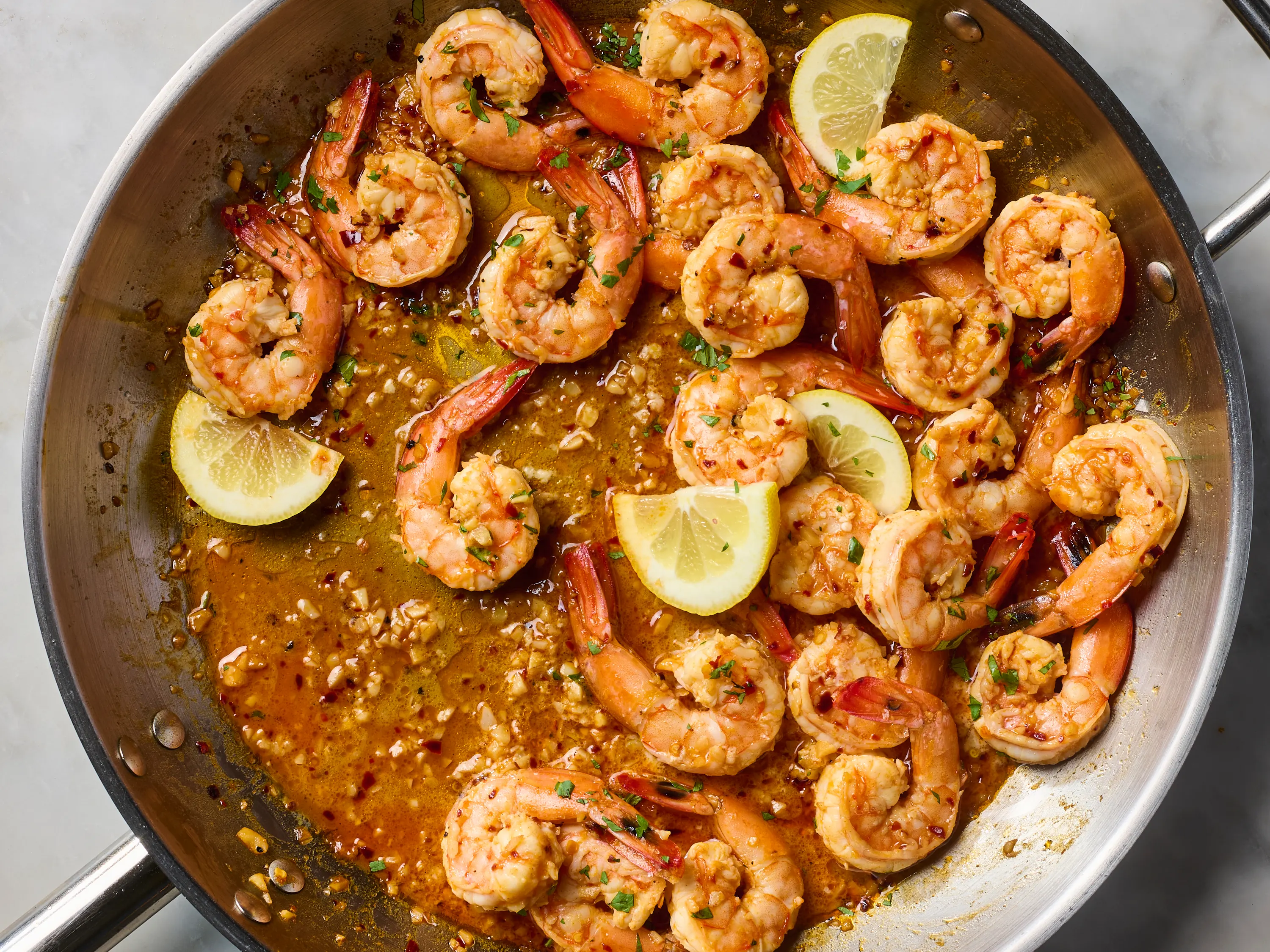 Peeled raw shrimp in a bowl next to whole lemons, a small dish of lemon zest, and minced garlic on a wooden cutting board