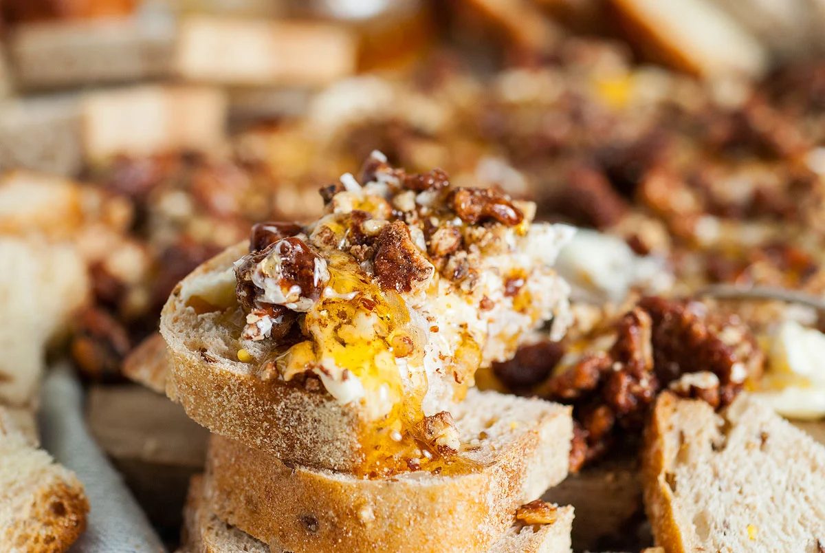 Praline pecans scattered on a wooden cheese board beside wedges of cheese and fresh fruit
