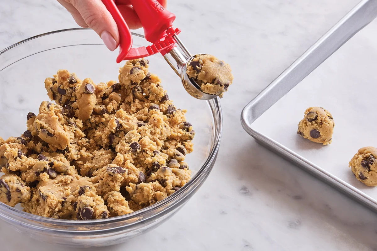 Rounded scoops of chocolate chip cookie dough spaced on a parchment-lined baking sheet, ready to chill before baking