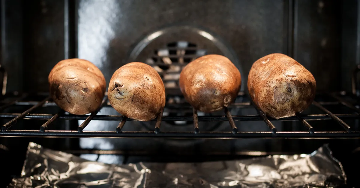 Russet potatoes baking directly on an oven rack with a sheet pan underneath to catch drips