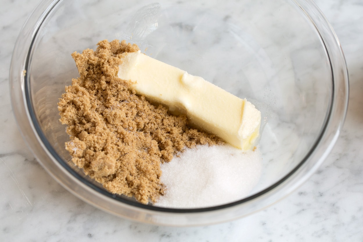Softened butter and brown sugar being mixed in a large bowl until fluffy, with a silicone spatula scraping down the sides