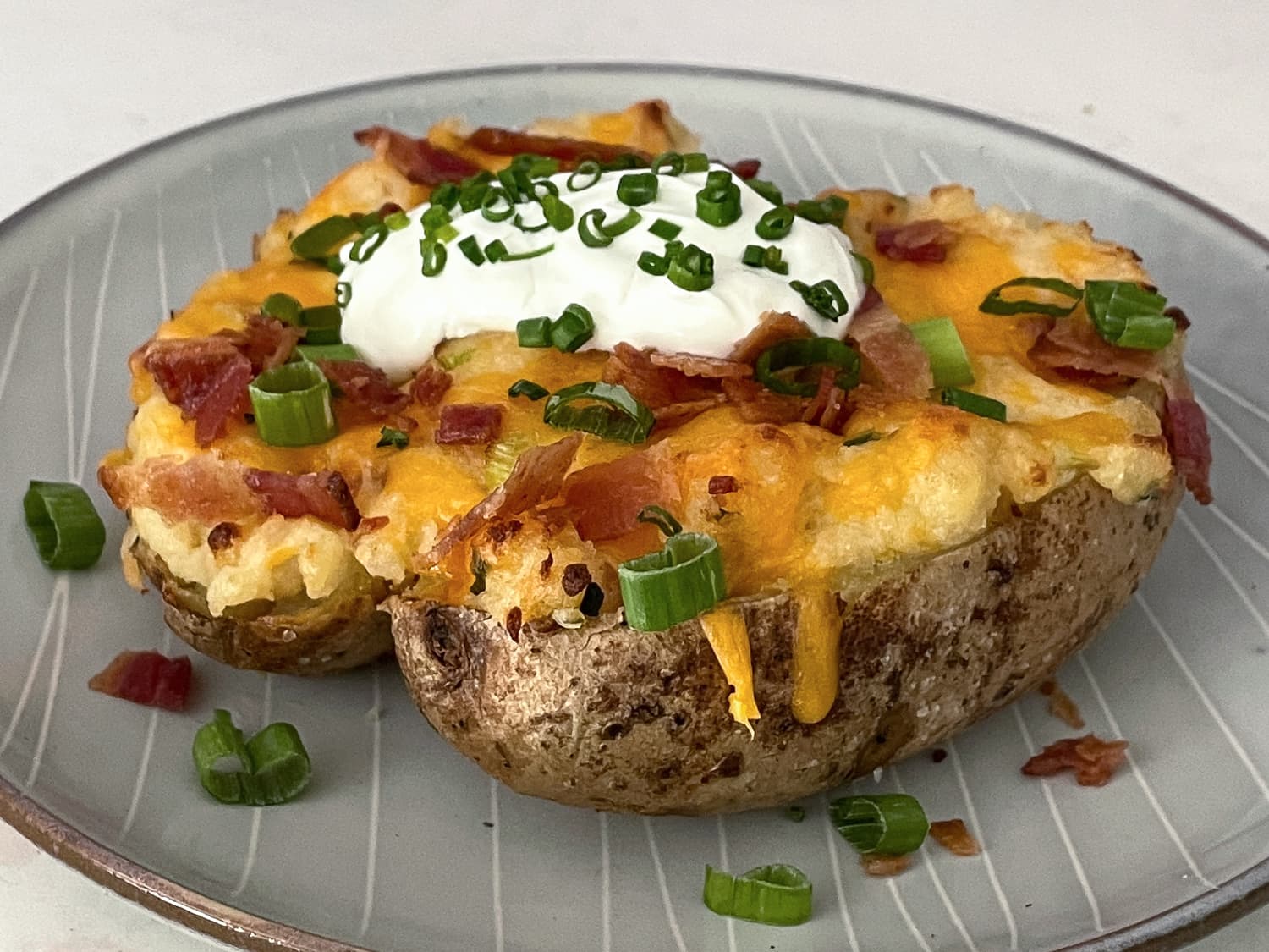 Split baked potato topped with butter, sour cream, chopped chives, and cracked black pepper on a plate