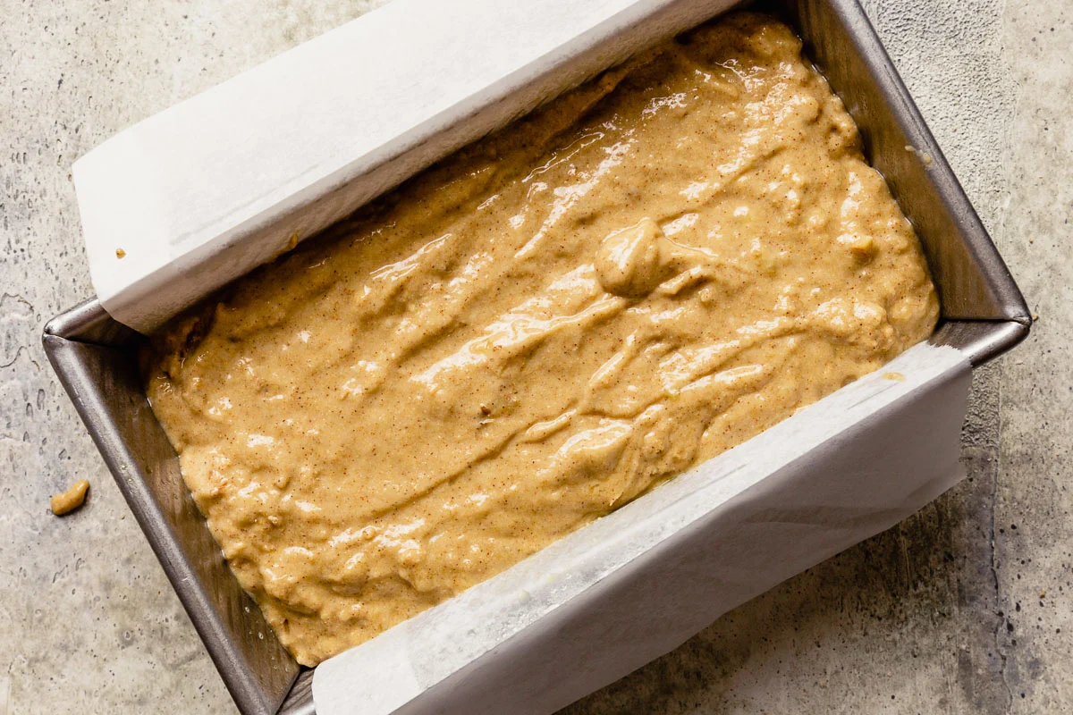 Thick banana bread batter spooned into a parchment-lined loaf pan on a kitchen counter, ready to bake