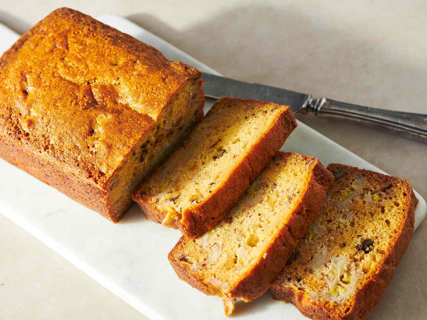 Thick slices of banana bread on a wooden cutting board, showing a moist crumb with a few walnut pieces, in natural window light