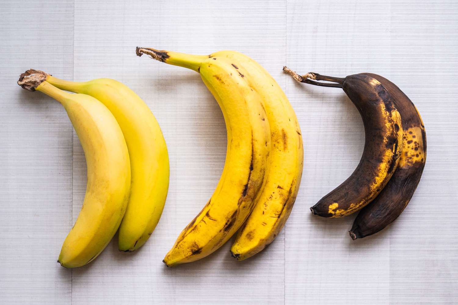 Three very ripe bananas with deeply speckled peels resting on a kitchen counter next to a mixing bowl